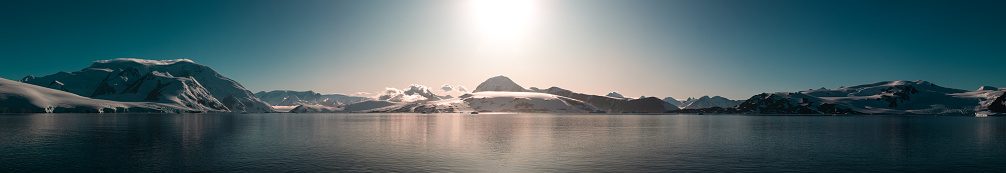 A panorama of a sunrise in Antarctica over snow clad mountains.