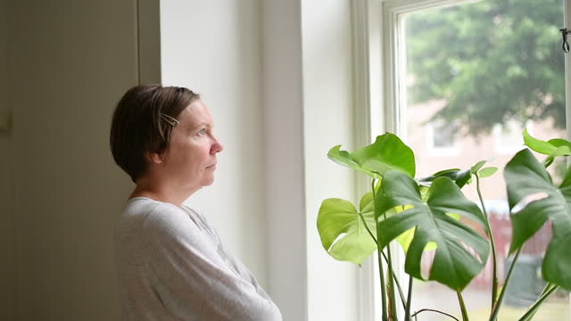 Introspective mid-adult female person looking out the window and contemplating