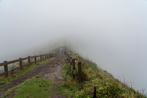 Small group of tourists on footpath in the fog over the caldera on Faial island, Azores