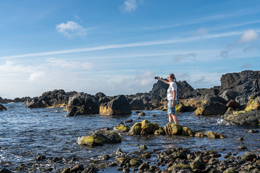 One women wading the sea at volcanic rock protruding out of the sea, close to the Mosteiros on Sao Miguel, and takin photos, Azores