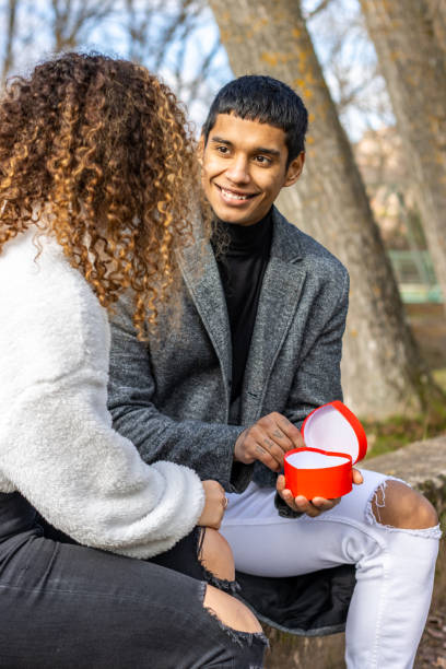 istock Young latin man proposing to his girlfriend outdoors. Sitting guy making marriage proposal to smiling girlfriend 1497969153