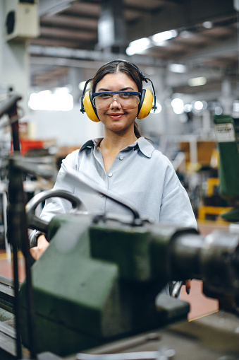 Portrait of hard working female industry technical worker or engineer woman confident serious face turner standing works on automatic universal cnc vertical milling machine for production of metal structures in an industrial manufacturing factory company. XXXL