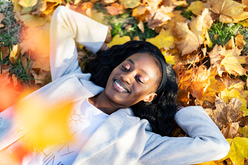 Young adult black woman lying down in yellow autumn leaves