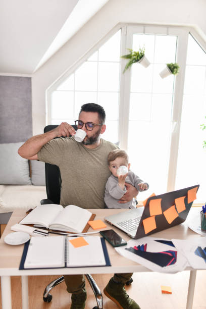 istock Male Designer Drinking Coffee While Baby Boy Drinks Water In Office 1497971728