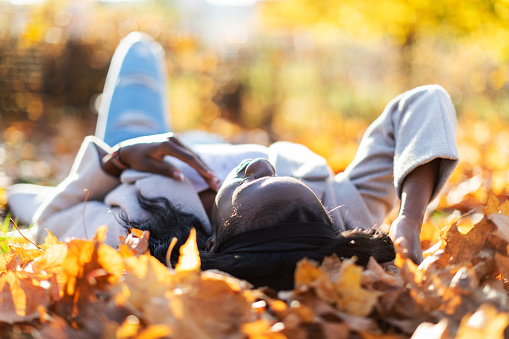Young adult black woman lying down in autumn leaves and relaxing