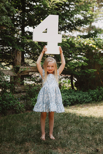 A beautiful little girl who is four years old, holds a number four.