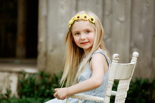 A beautiful little girl who is four years old, looks at the camera as she sits in an antique chair.