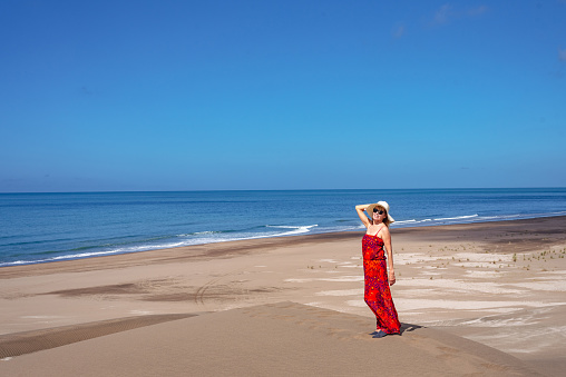 Mature woman smiling while posing standing in the top of a dune at the beach. Summer concept.