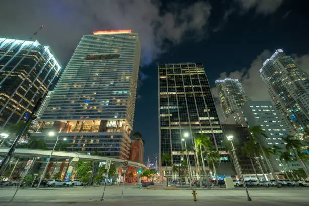 Downtown district of of Miami Brickell in Florida, USA. Brightly illuminated high skyscraper buildings and street with car trails and metrorail traffic in modern american midtown.