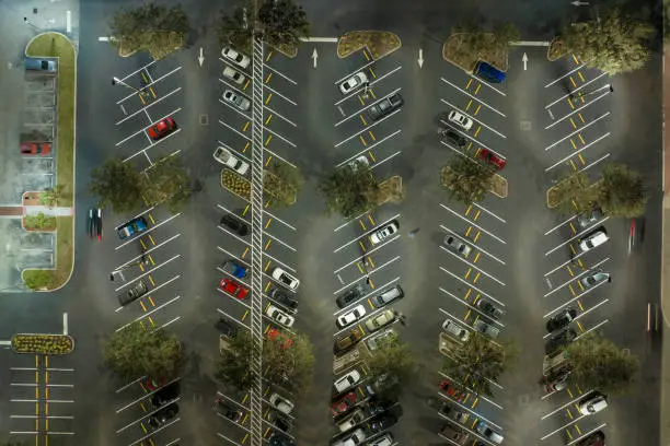 Aerial view of large parking lot at nighttime with many parked cars. Dark carpark at supercenter shopping mall with lines and markings for vehicle places and directions.