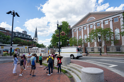 Cambridge, MA, USA - June 29, 2022: A Harvard campus tour group guided by a Harvard student is seen gathering outside the Harvard MBTA Station in Cambridge, Massachusetts.