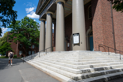 Cambridge, MA, USA - June 29, 2022: A student walks past the Memorial Church of Harvard University, in the center of the Harvard Yard, in Cambridge, Massachusetts.