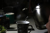 Kettle pouring into mug. Kettle pouring boiling water into a cup during breakfast in morning. Dark night. Out of focus