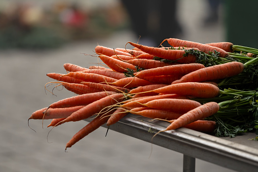 Picture of carrots, orange, stacked, unpeeled, raw, ready to be prepared, on a german green farmers market.