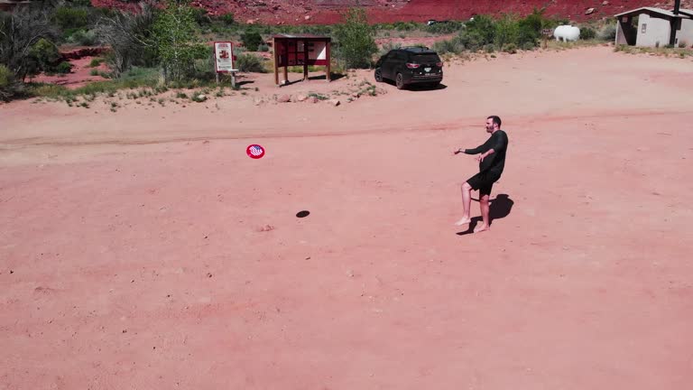 From above, a tall man with dark hair and a neat beard plays frisbee barefoot in the red dirt of Mineral Canyon near Dead Horse Point and Canyonlands National Park.