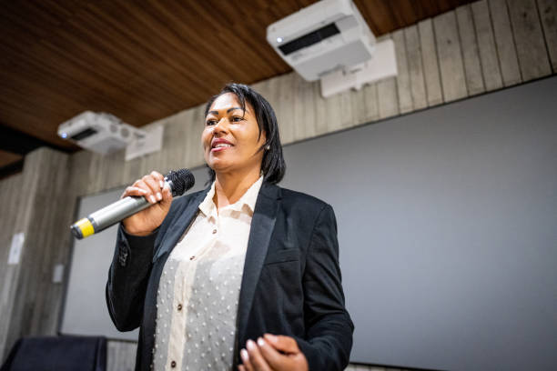 femme mûre parlant au micro dans un séminaire - interview meeting business women photos et images de collection