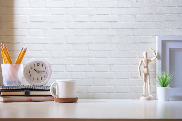 istock A cup of coffee, clock, picture frame and pencil holder on white table against brick wall. 1498002257