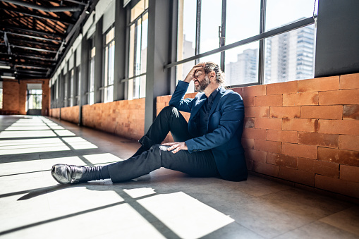Worried mature businessman sitting on ground at office