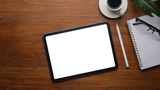 istock Digital tablet with white screen, coffee cup, glasses and notepad on wooden office desk. 1498003614