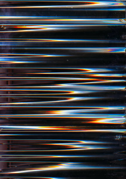 A close-up abstract image featuring glass strips arranged diagonally and blue round shapes behind it. Light creates rainbow reflections and glossy highlights, suggesting modern design, technology, and futuristic aesthetics.