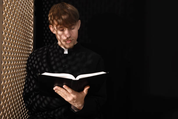 sacerdote católico con la biblia cerca de la ventana de madera en el confesionario. espacio para texto - confession booth church forgiveness wood fotografías e imágenes de stock