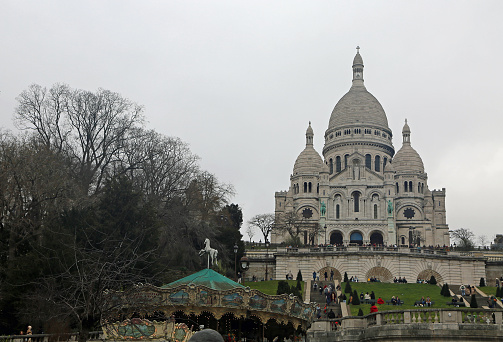 View of the Basilique du Sacre-Coeur during a sunny day in Paris, France. The Basilica is located at the highest point of the city in the heart of Montmartre district. The basilica and its surroundings are a popular location for tourists that visit Paris.