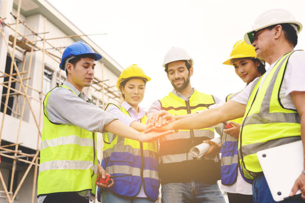 istock Group of contractors, engineers and formats in safety vests with helmets join hands to work together to successfully complete a construction project on construction site. cooperation and success concept. 1498035108
