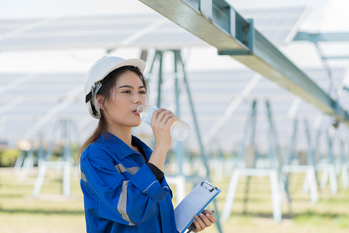 Female engineer worker drinking water during working in solar panels power farm. Technician working at solar power station