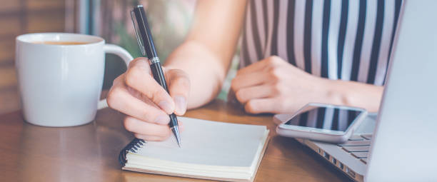 istock Woman hand is writing on a notepad with a pen on a wooden desk. 1498045526