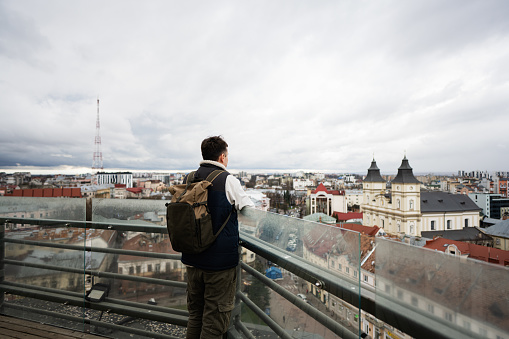 Back view of man tourist with backpack stand on background of panorama view city.