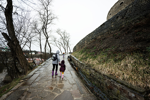 Mother and girls walk up the wet path to an ancient medieval castle fortress in rain.