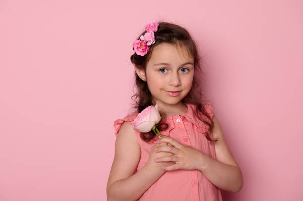 Authentic Caucasian beautiful elegant little girl in pink dress, holding a rose flower, smiling cutely looking at camera Authentic Caucasian child, beautiful elegant little girl in pink dress, holding a rose flower, smiling cutely looking at camera, isolated pink background. Copy space. Kids beauty and fashion portrait cutely stock pictures, royalty-free photos & images