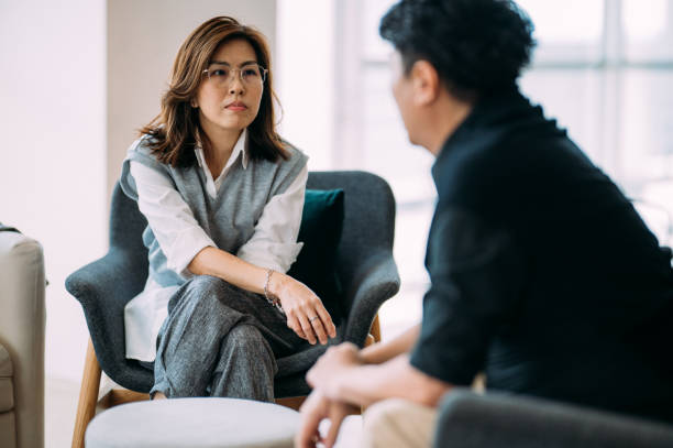Navigating Challenges: A Therapeutic Dialogue between an Asian Female Psychologist and a Mature Man - Consulting Patient at Modern Office stock photo