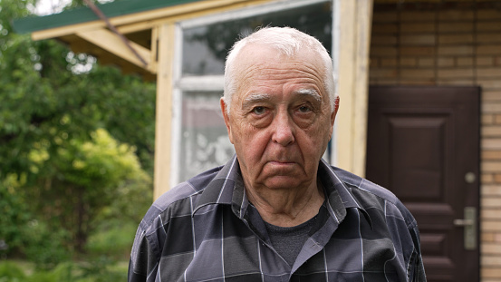 Portrait of a serious elderly man in the suburbs. Male senior person looks thoughtfully into the camera. The pensioner feels loneliness and the experience of the past years.