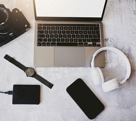 In an office, a shot was taken of a mobile phone, laptop, camera, power bank, watch, timepiece, and headphones all nicely placed on a desk. Stock photo