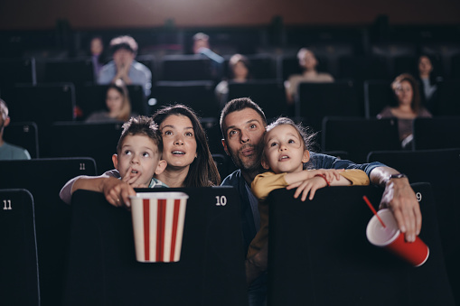 Young family enjoying while watching a movie in cinema. Focus is on parents.