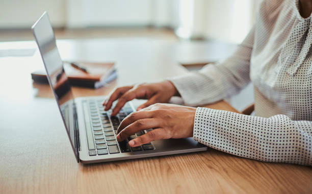 uma empresária não reconhecida sentada em sua mesa, digitando em seu laptop. foto de stock - unrecognized person - fotografias e filmes do acervo