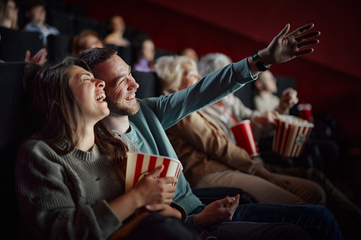 Cheerful couple having fun while laughing during a comedy movie in cinema. Focus is on man.