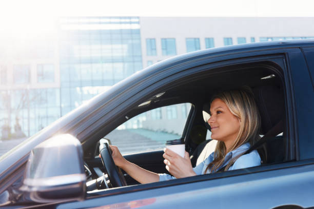 istock Smiling woman drinking coffee while driving a car. 1498067179