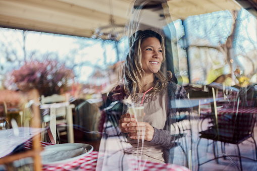 Young happy woman enjoying while day dreaming in a restaurant. The view is through glass.