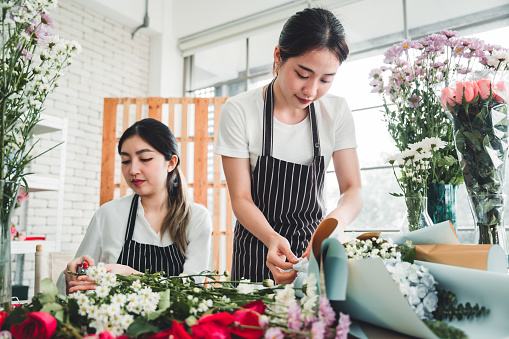 Two beautiful florists are meticulously arranging a bouquet of flowers ready to be sent to a client and to show in the shop and to attract customers in the flower shop.