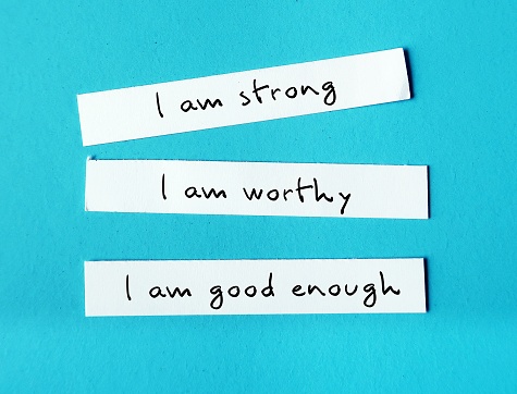 Three note paper on blue background with handwritten text I AM STRONG, I AM WORTHY, I AM ENOUGH - powerful self talk positive affirmations to boost self confidence self esteem