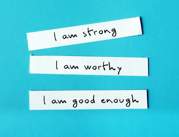 Three note paper on blue background with handwritten text I AM STRONG, I AM WORTHY, I AM ENOUGH - powerful self talk positive affirmations to boost self confidence self esteem