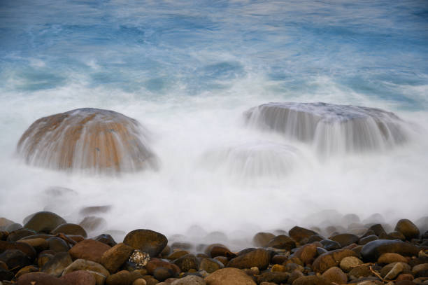 White waves flow slowly from the rocks into the sea. Slow exposure shot. View of Keelung Harbor from Wanli Beach in New Taipei City. Taiwan.
