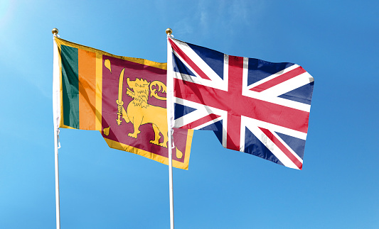 Flags of Sri Lanka and United Kingdom against cloudy sky. waving in the sky