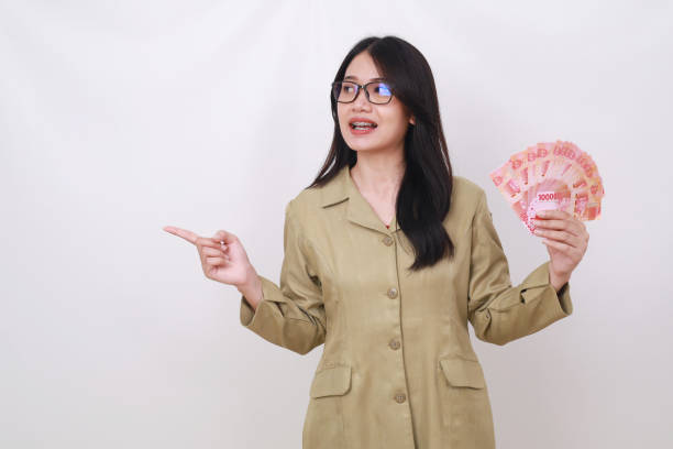 istock Attractive civil servant woman holding Indonesian banknotes while pointing sideways 1498081417