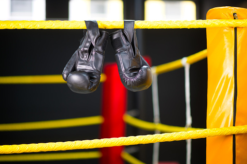 Ringside Black Boxing gloves hanging from ropes in a boxing ring with red boxing pads in a boxing gym no people, Cape Town, South Africa