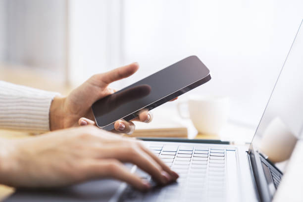 istock Woman expertly using a cutting-edge smartphone at her workspace, laptop on standby against the vague backdrop of a thriving office 1498082838
