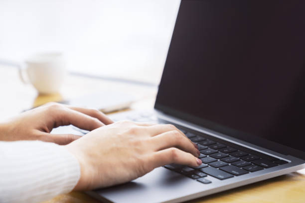 この画像は、ぼやけたオフィスの背景に設定された洗練されたラップトップキーボードで入力する女性の手を詳細にキャプチャしています - mail keyboard button ストックフォトと画像