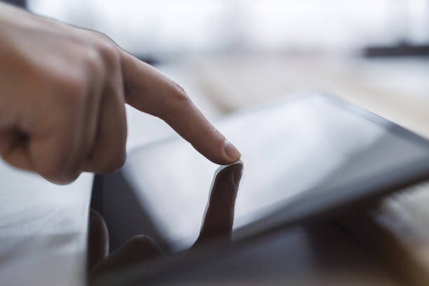 istock Man's fingertip gently tapping the screen of a modern digital tablet lying on a desk, surrounded by the unfocused brightness of a contemporary office space 1498083474
